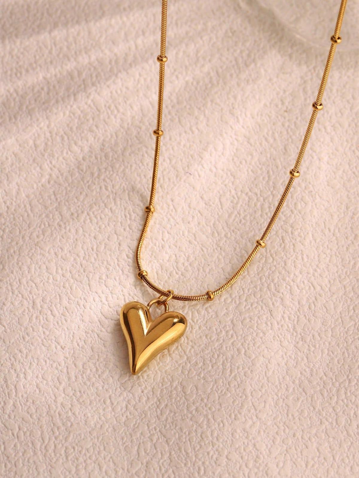 Gold heart pendant necklace on a stainless steel anti-tarnish chain displayed on a beige jewelry stand.