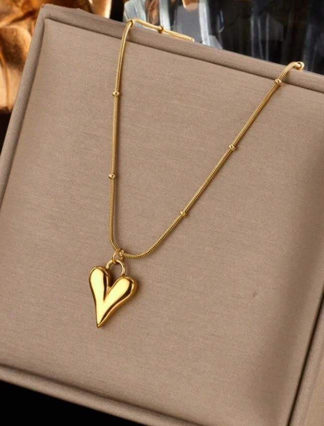 Gold heart pendant necklace on a stainless steel anti-tarnish chain displayed on a beige jewelry stand.